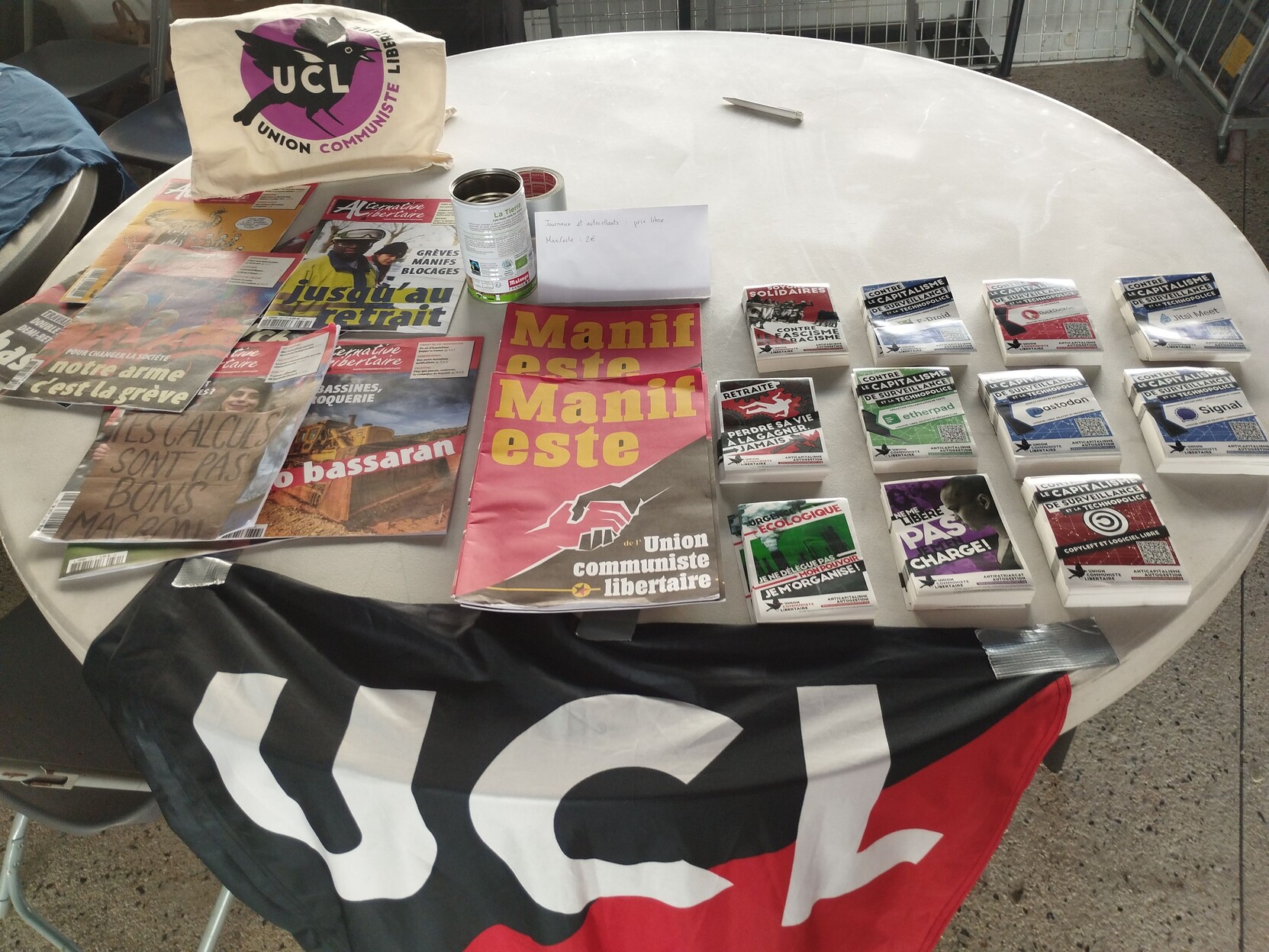 Photo de la table UCL avec les stickers à l'effigie de logiciels libres de notre campagne contre le capitalisme de surveillance et la technopolice, nos manifestes, nos journaux.